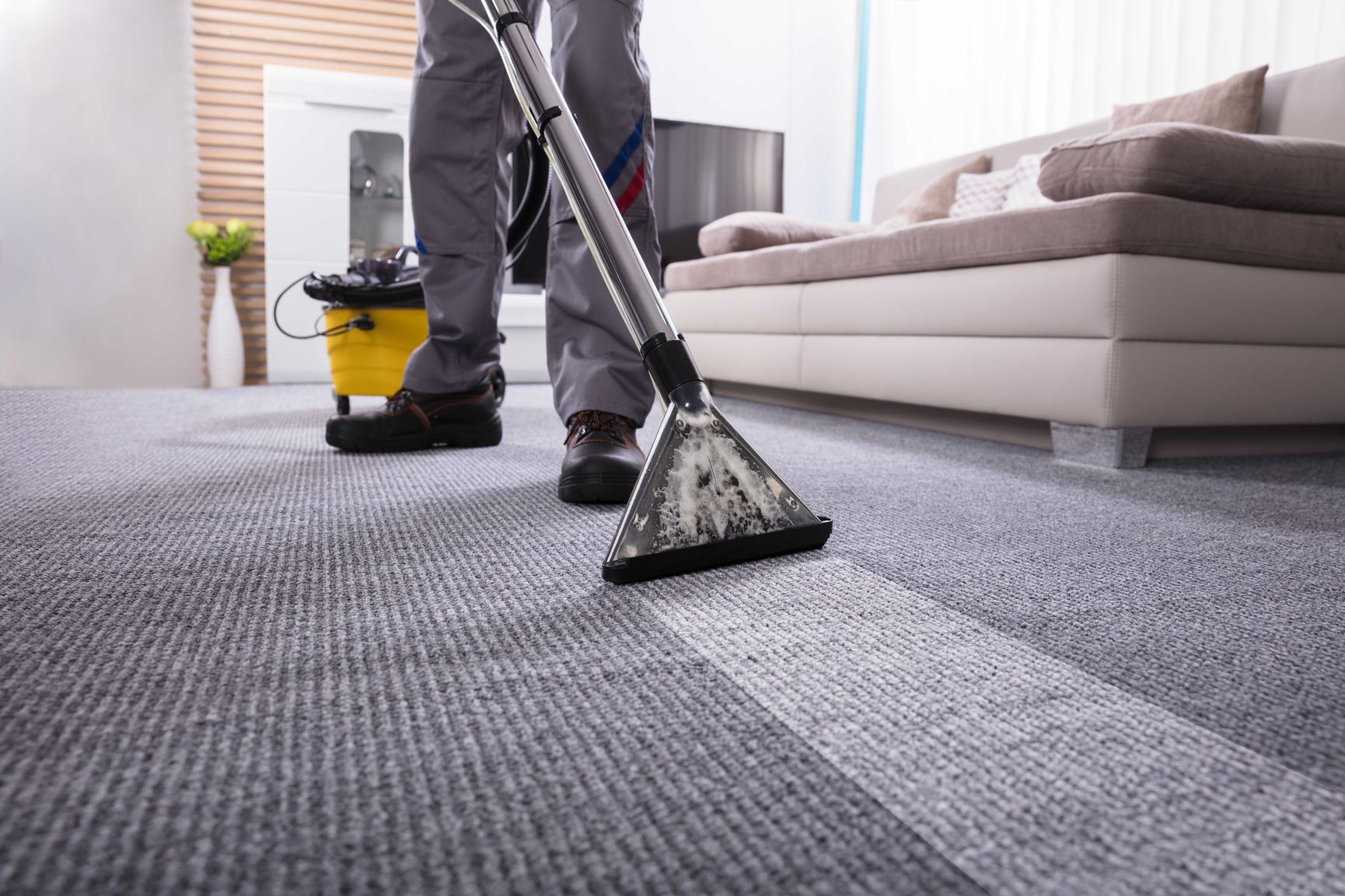 Reinigungskraft reinigt grauen Teppichboden mit professioneller Nassreinigungsmaschine