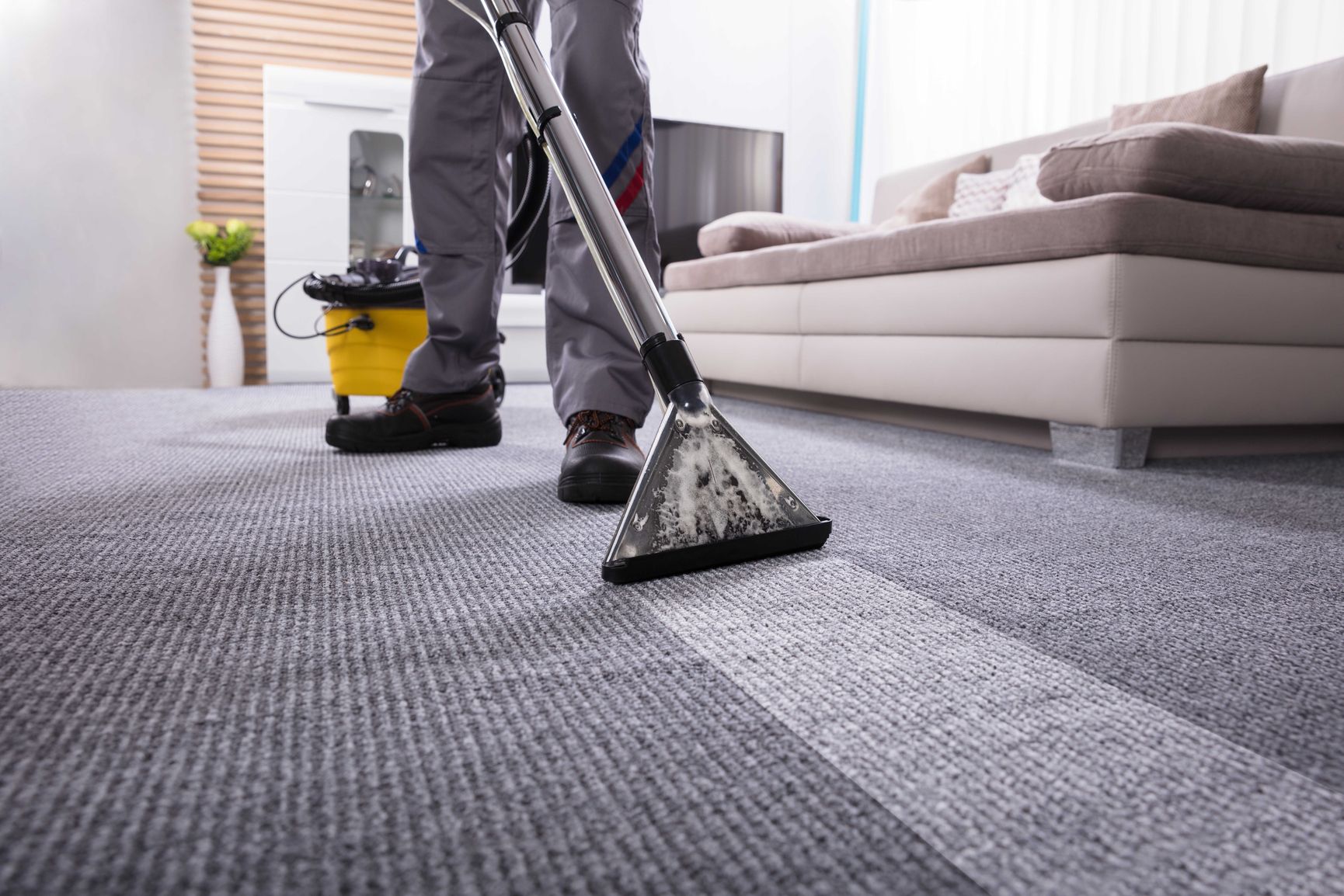 Reinigungskraft reinigt grauen Teppichboden mit professioneller Nassreinigungsmaschine