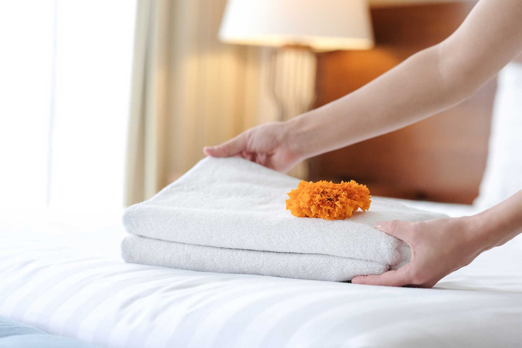 Mitarbeiterin legt frisches gefaltetes Handtuch auf ein Hotelbett