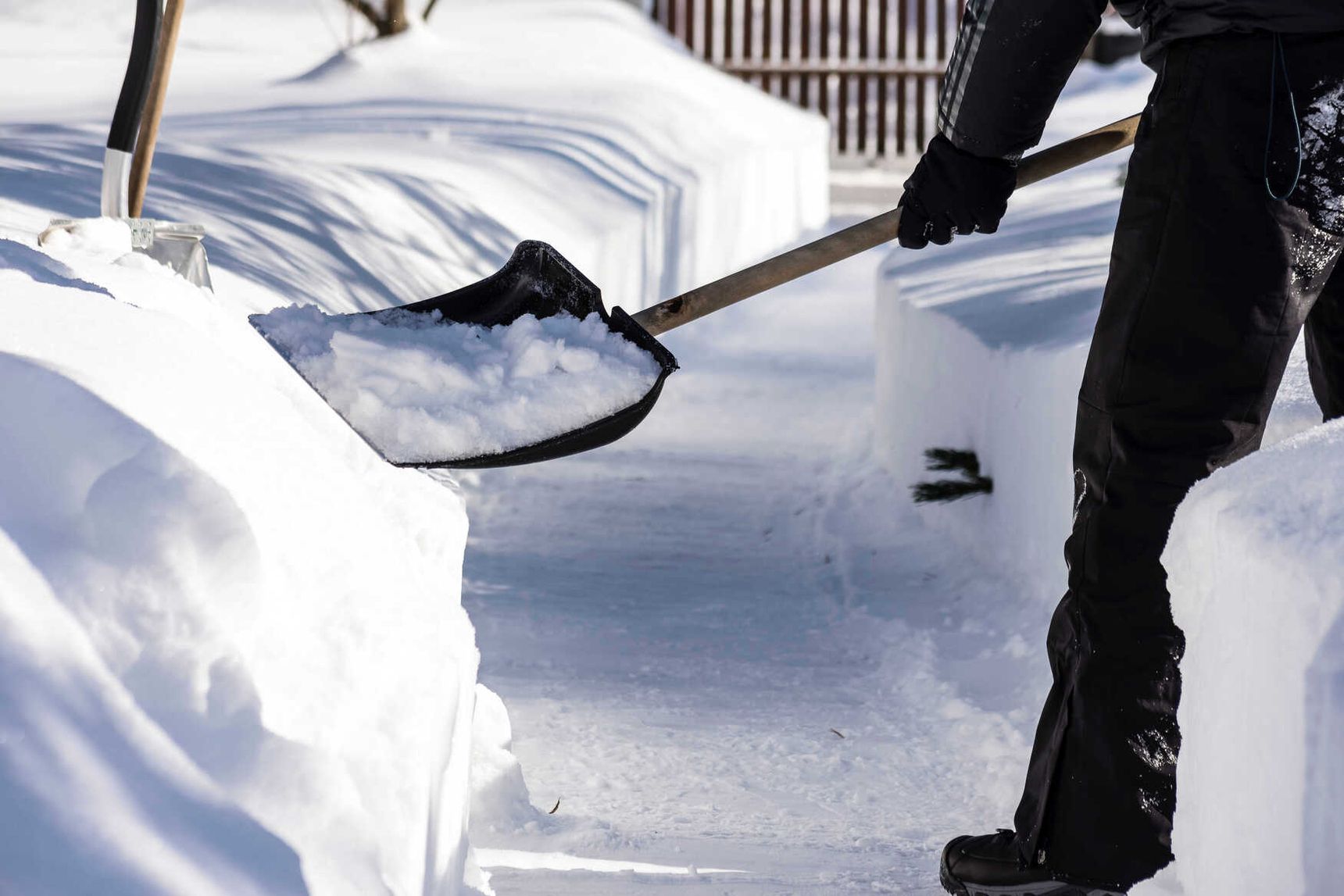 Mitarbeiter räumt Schnee mit einer Schneeschaufel vom Gehweg